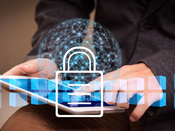 Eine Person hält ein Tablet in den Händen; darüber liegt eine grafische Darstellung aus Netzwerklinien und einem großen Schloss-Symbol, das digitale Sicherheit veranschaulicht.